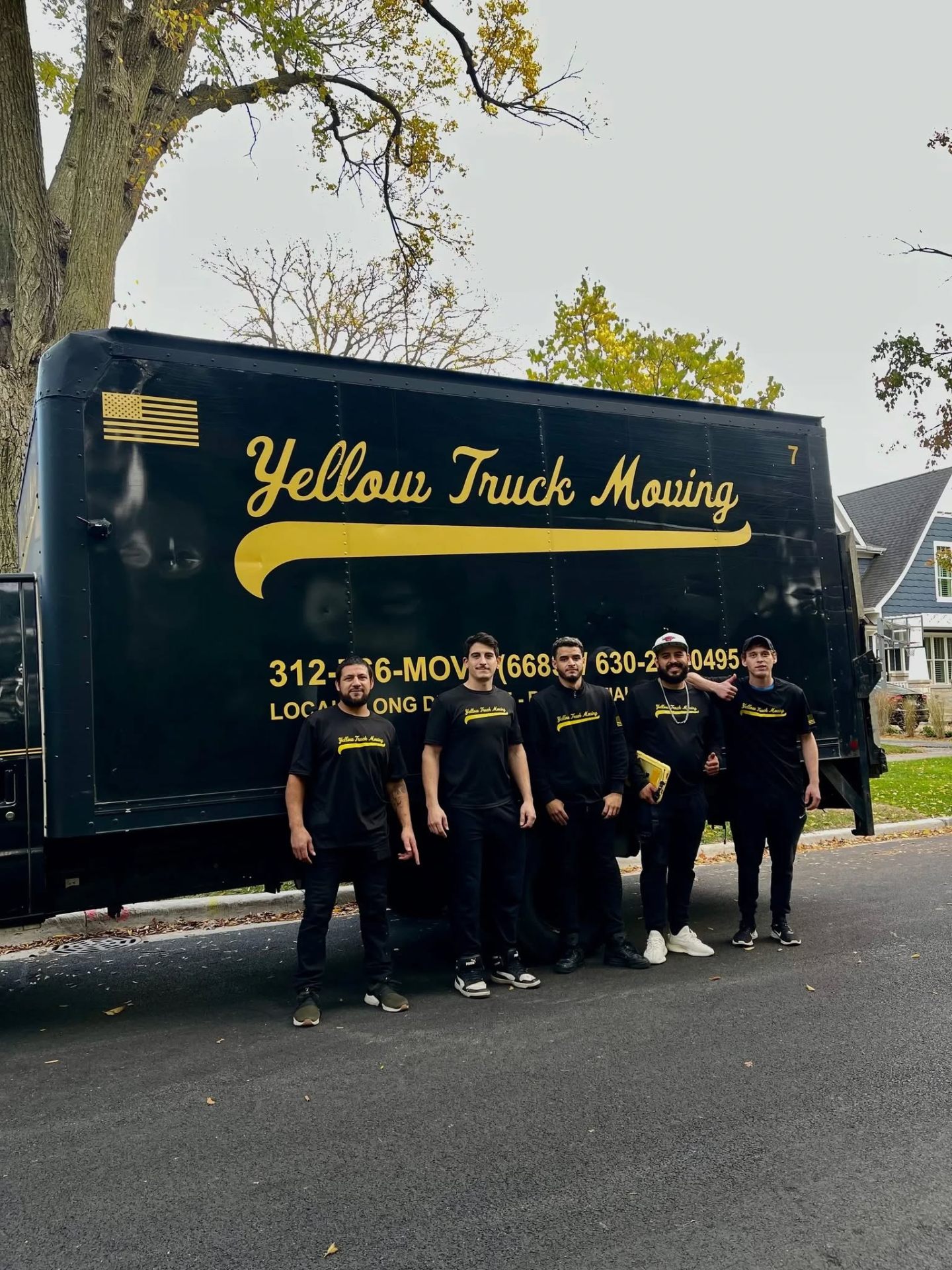 Yellow Truck Moving crew of five standing in front of the black-and-gold branded box truck
