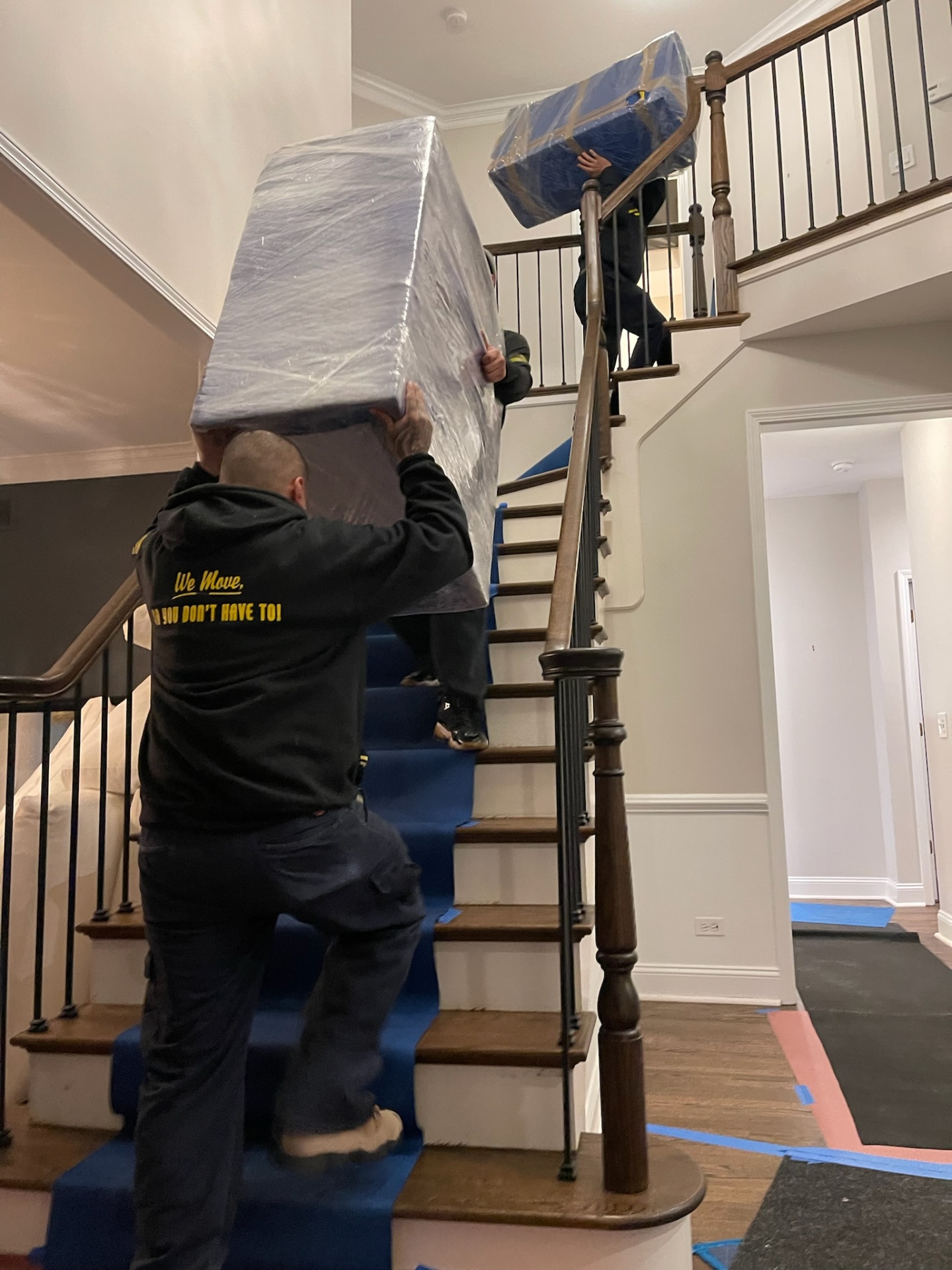 Two Yellow Truck Moving movers carrying wrapped furniture up a residential staircase