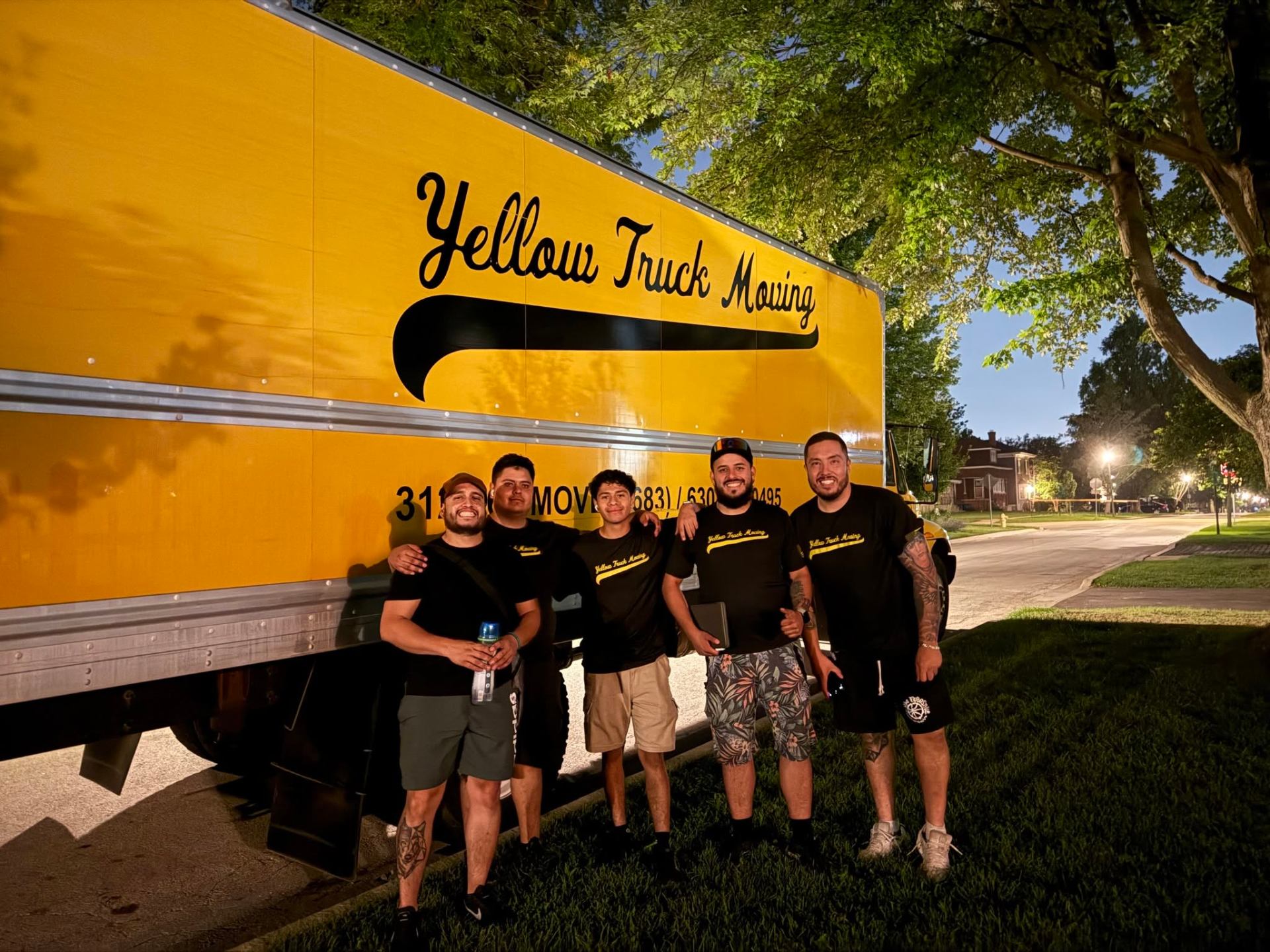 Yellow Truck Moving team of five posing in front of a yellow moving truck at dusk