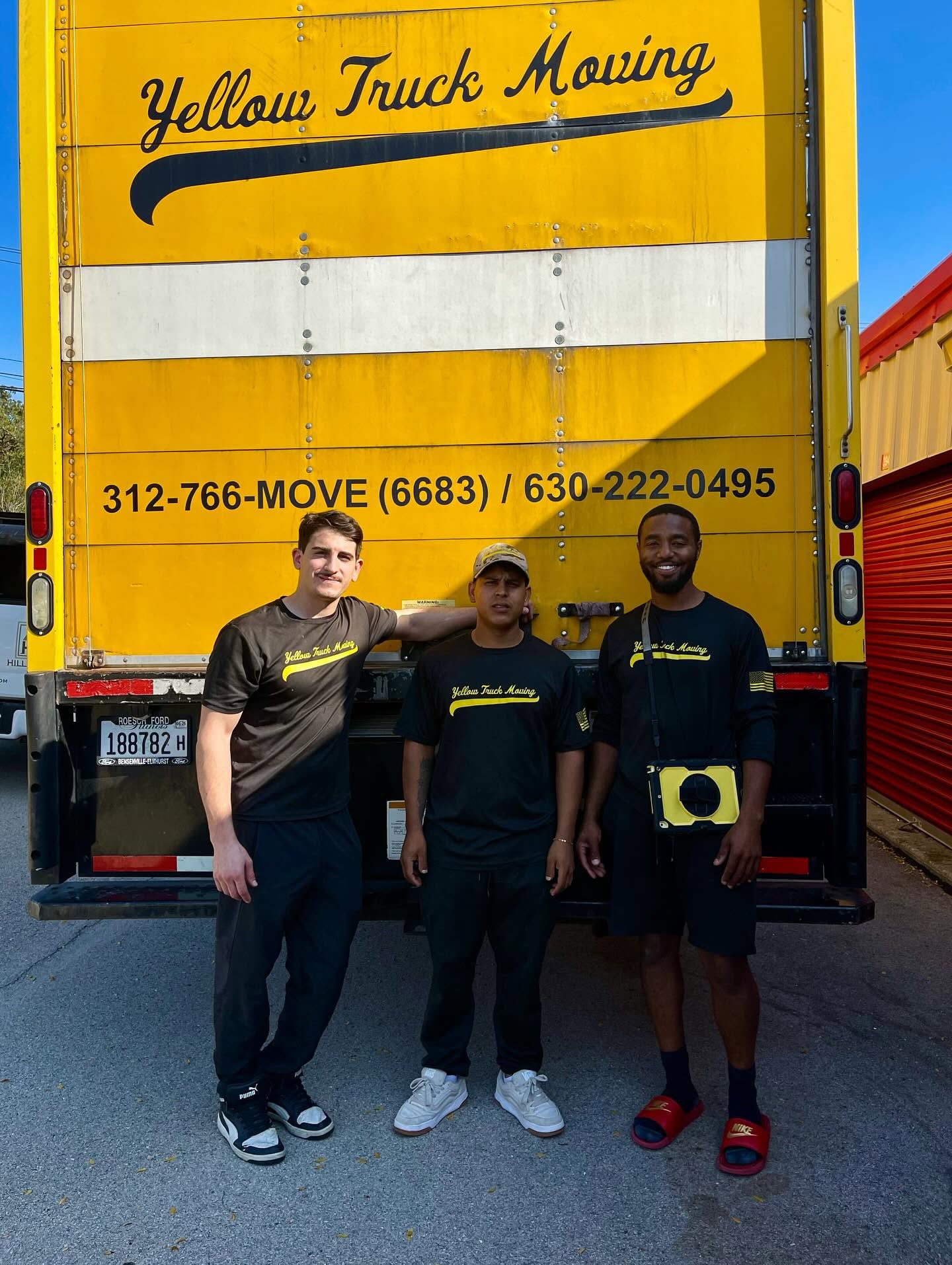 Three Yellow Truck Moving crew members standing behind a yellow box truck